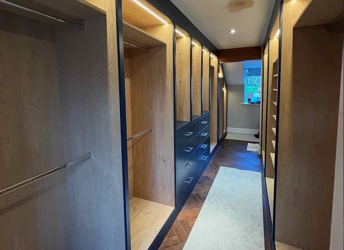 Walk-in dressing room with oak-veneer shelving, drawers and a herringbone wood floor