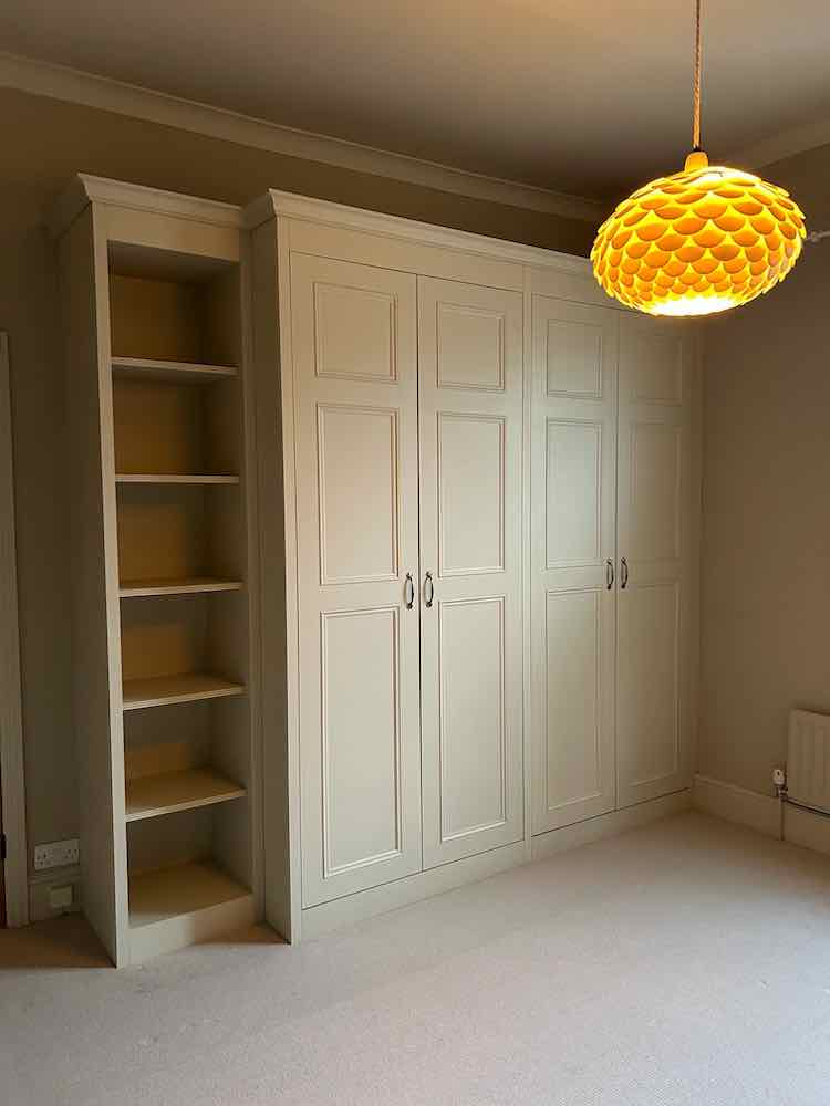 Cream four-door fitted wardrobe built alongside open bookshelving
