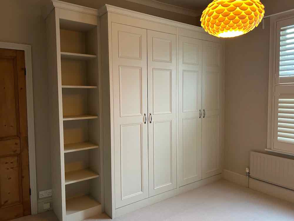 Cream fitted wardrobe and bookcase spanning the full length of a bedroom wall